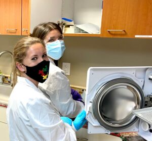 Two women in lab coats and masks are holding a washer.
