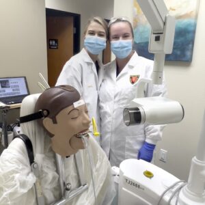 Two women in white lab coats and a dummy