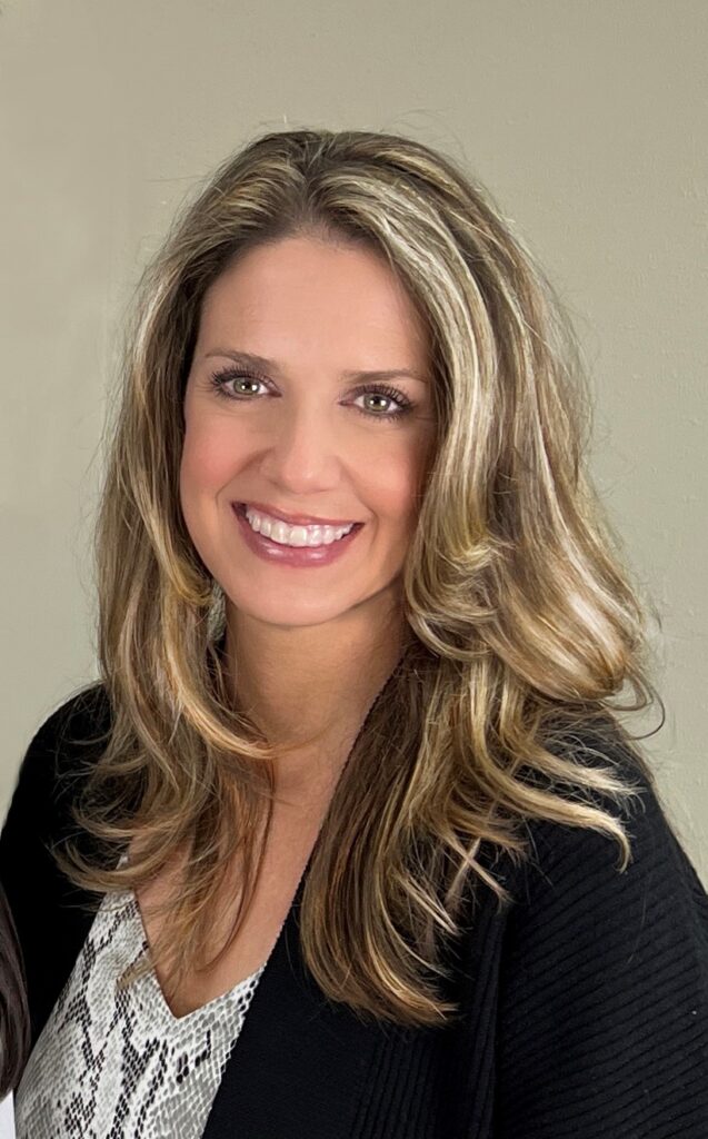 A woman with long hair and brown eyes smiling.